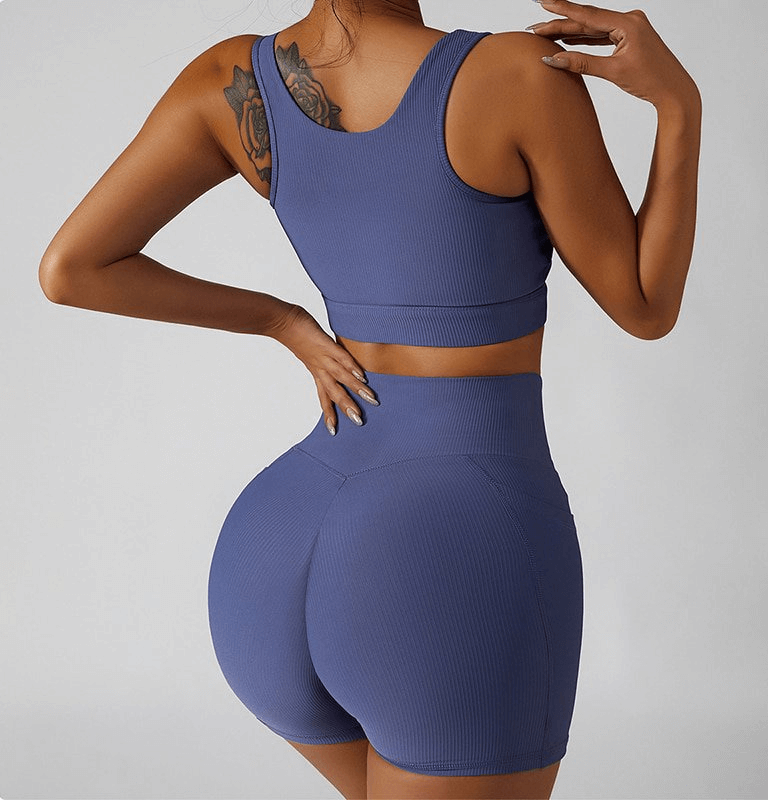 Back view of woman wearing purple athletic shorts and matching top, showcasing side pockets and elastic fit for yoga and fitness activities.